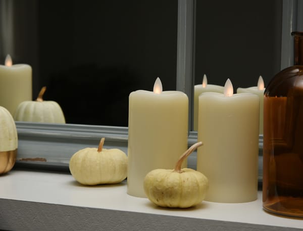large flameless candles sitting in a windowsill with miniature pumpkins