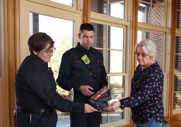 two firefighters showing an older adult a smoke alarm kit