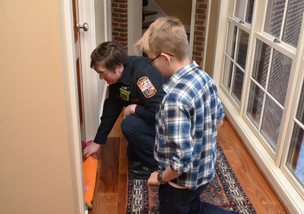 a firefighter showing a boy how to place a towel at the bottom of a door to keep smoke out