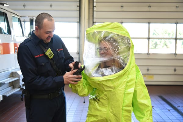 firefighter helping another firefighter take off a hazmat suit