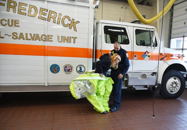 firefighter helping another firefighter take off a hazmat suit