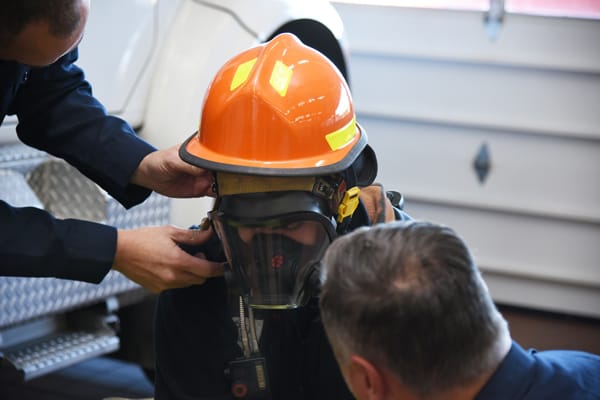 two firefighters helping another fit a face piece