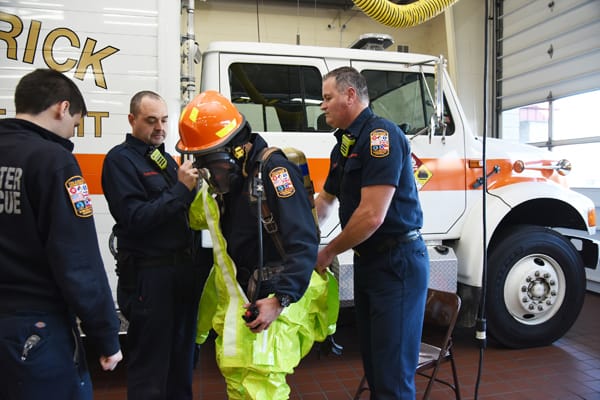 firefighters helping another remove a hazmat suit