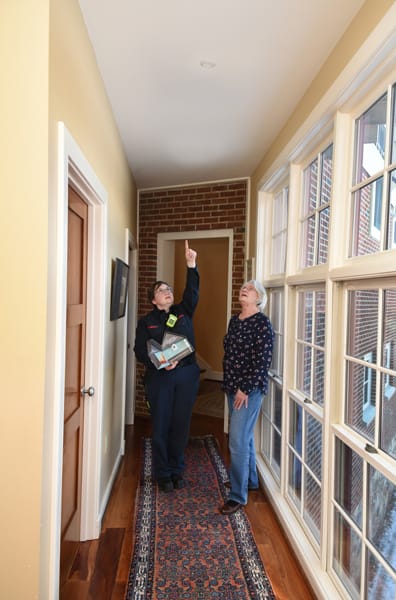 female firefighter standing beside woman and pointing to a sprinkler head on the ceiling