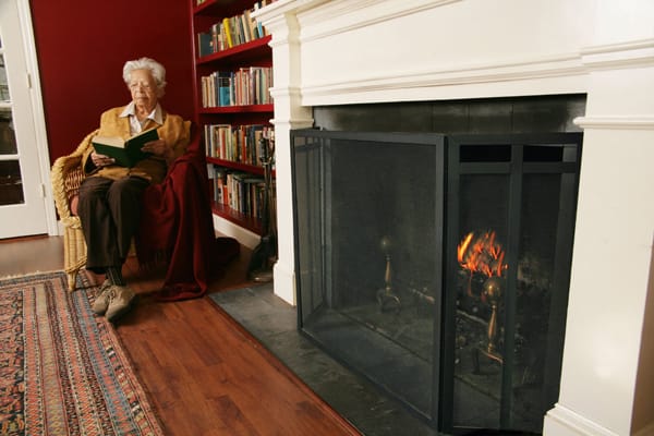older woman sitting next to a fireplace