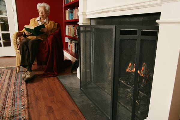 older woman sitting next to a fireplace
