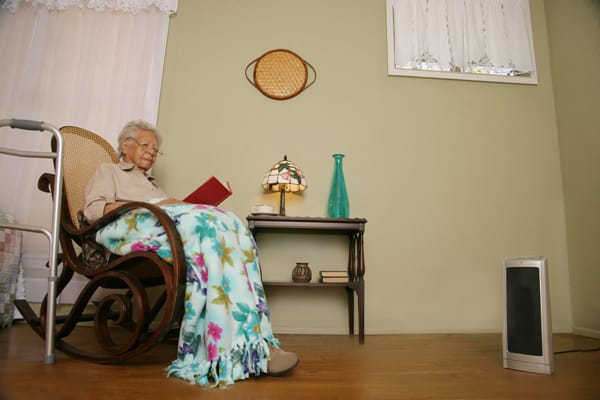 older woman sitting 3 feet away from a portable heater