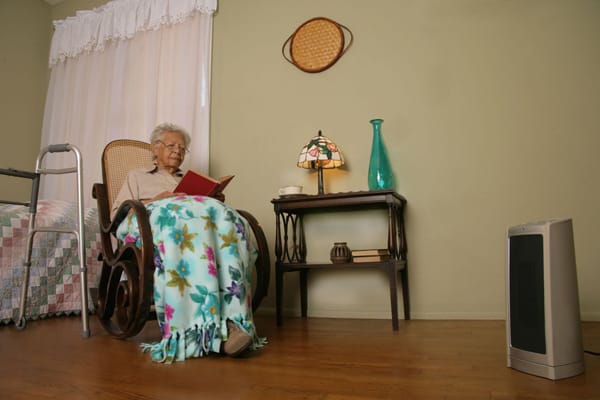 older woman sitting 3 feet away from a portable heater
