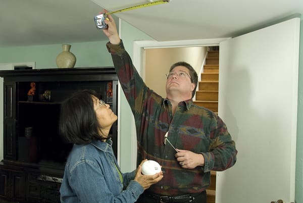 woman watching a man measure for a smoke alarm installation