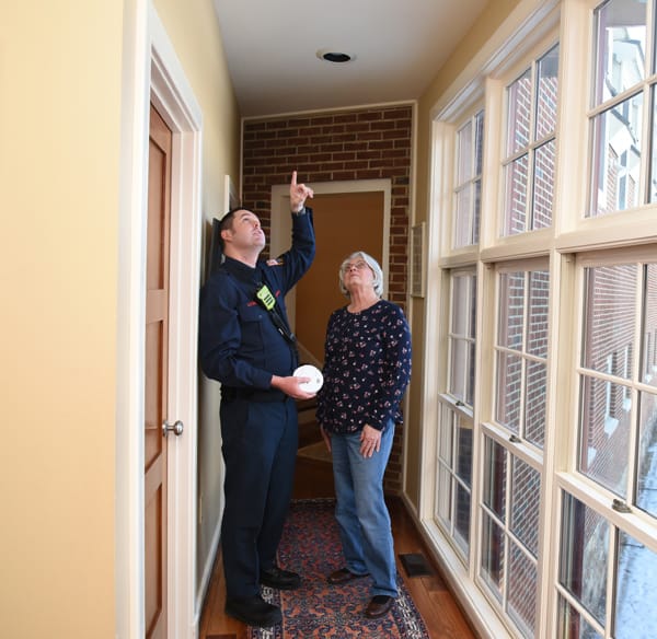 firefighter showing an older woman where to install a smoke alarm on the ceiling