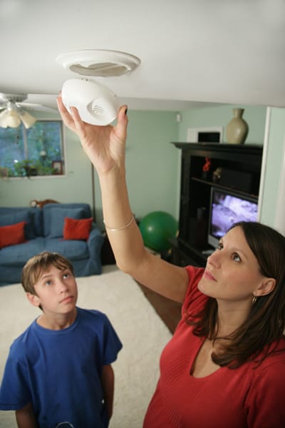 boy watching mom install a smoke alarm
