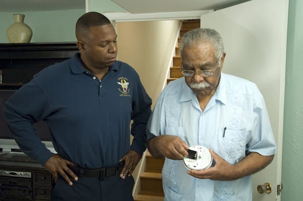 older man changing smoke alarm batteries while firefighter watches