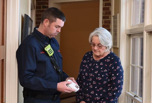 firefighter changing smoke alarm battery while older woman watches