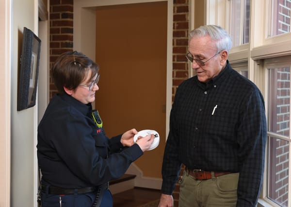 firefighter changing smoke alarm battery while older man watches