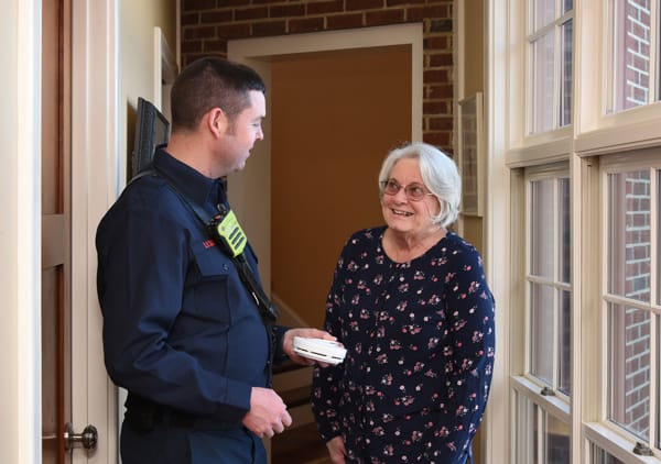 firefighter holding smoke alarm and talking with older woman