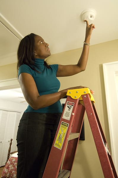 woman reaching up to test a smoke alarm