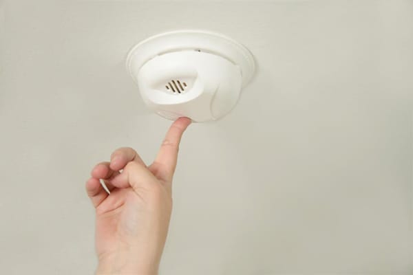 closeup of hand reaching up to test a smoke alarm