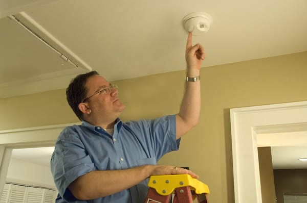 man on a ladder testing a smoke alarm