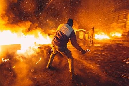 man throwing a Molotov cocktail with fire in the background