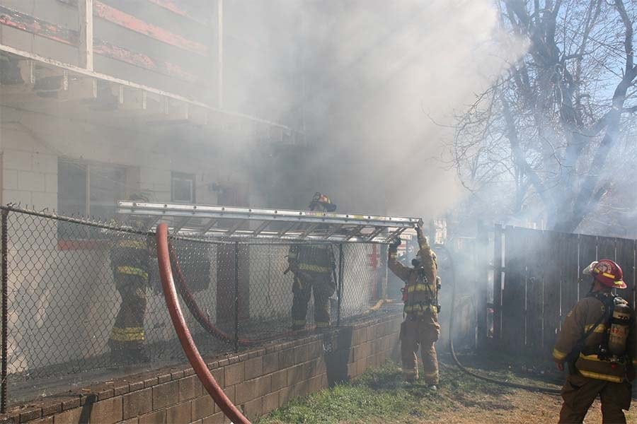 firefighters lifting a ladder as a house fire