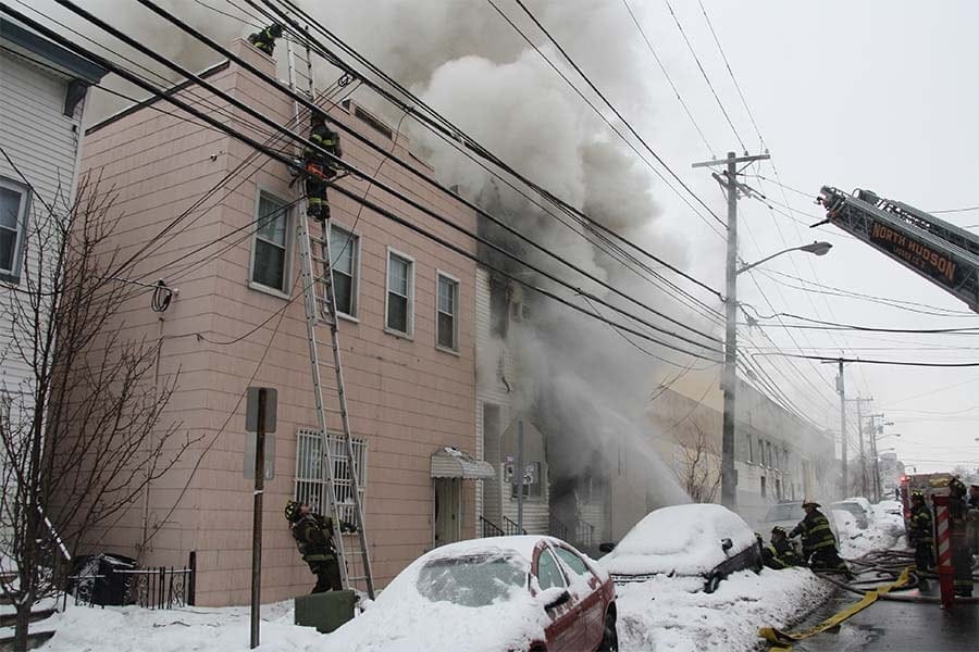 firefighters lifting a ladder as a house fire