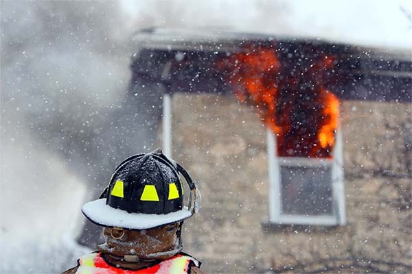 firefighter looking up at a window with fire coming out of it