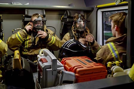firefighters putting on face pieces in cab