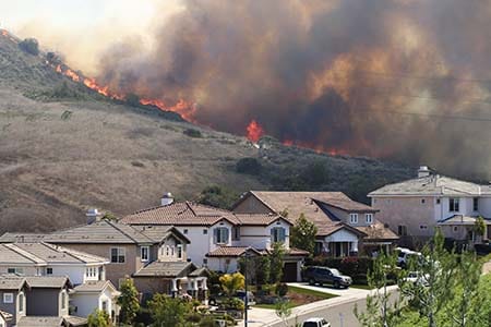 homes with wildfire in background on hillside